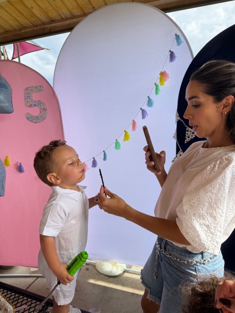 Na festa, uma mãe fotografa com o celular uma criança soprando uma velinha